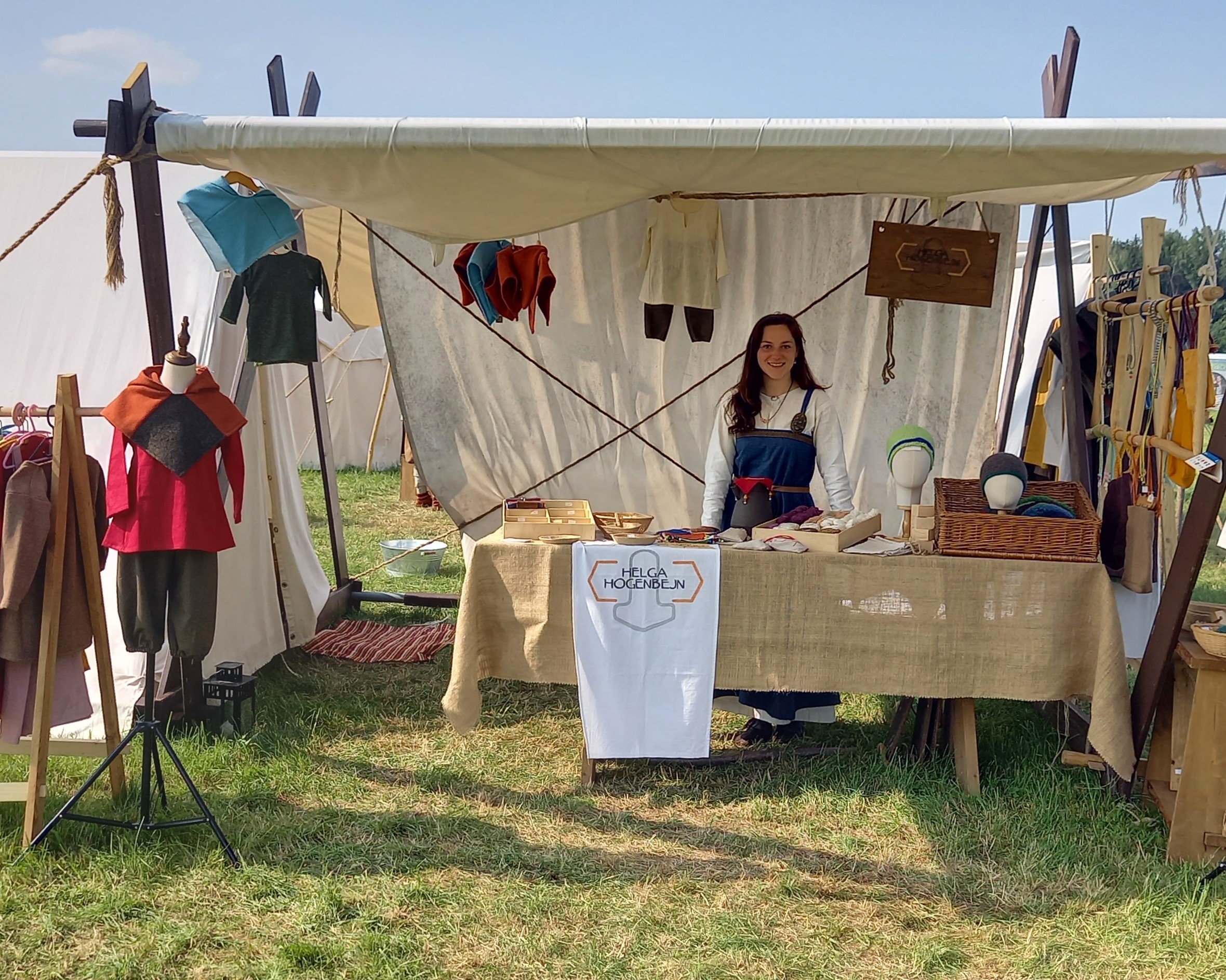 Mittelalter Marktstand mit Kinderkleidung und Frau hinter einem Tisch.